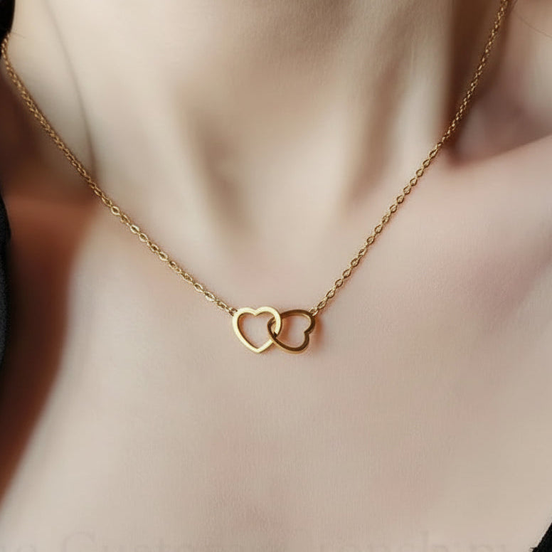 Gold necklace with interlocking heart pendants on a person wearing a black top.