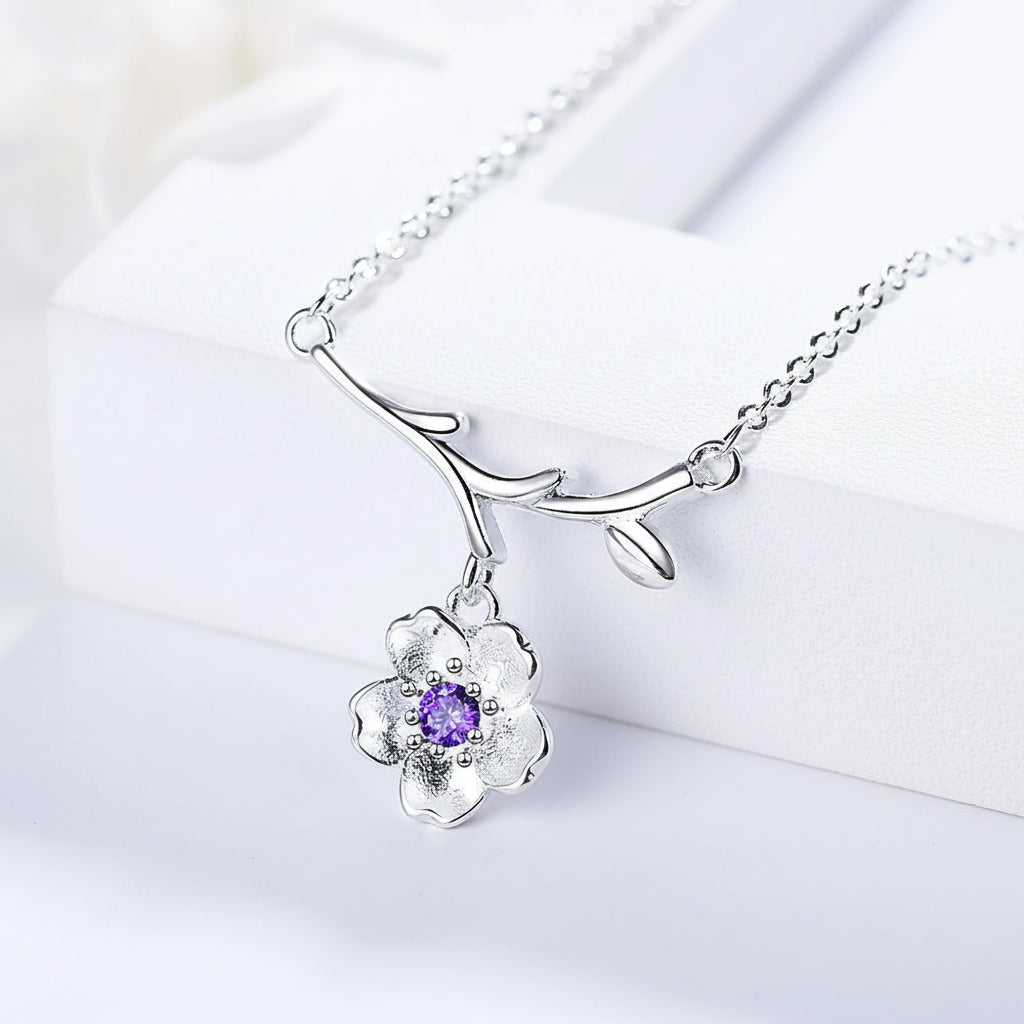 Silver necklace with a flower pendant featuring a purple gemstone on a light blue background.